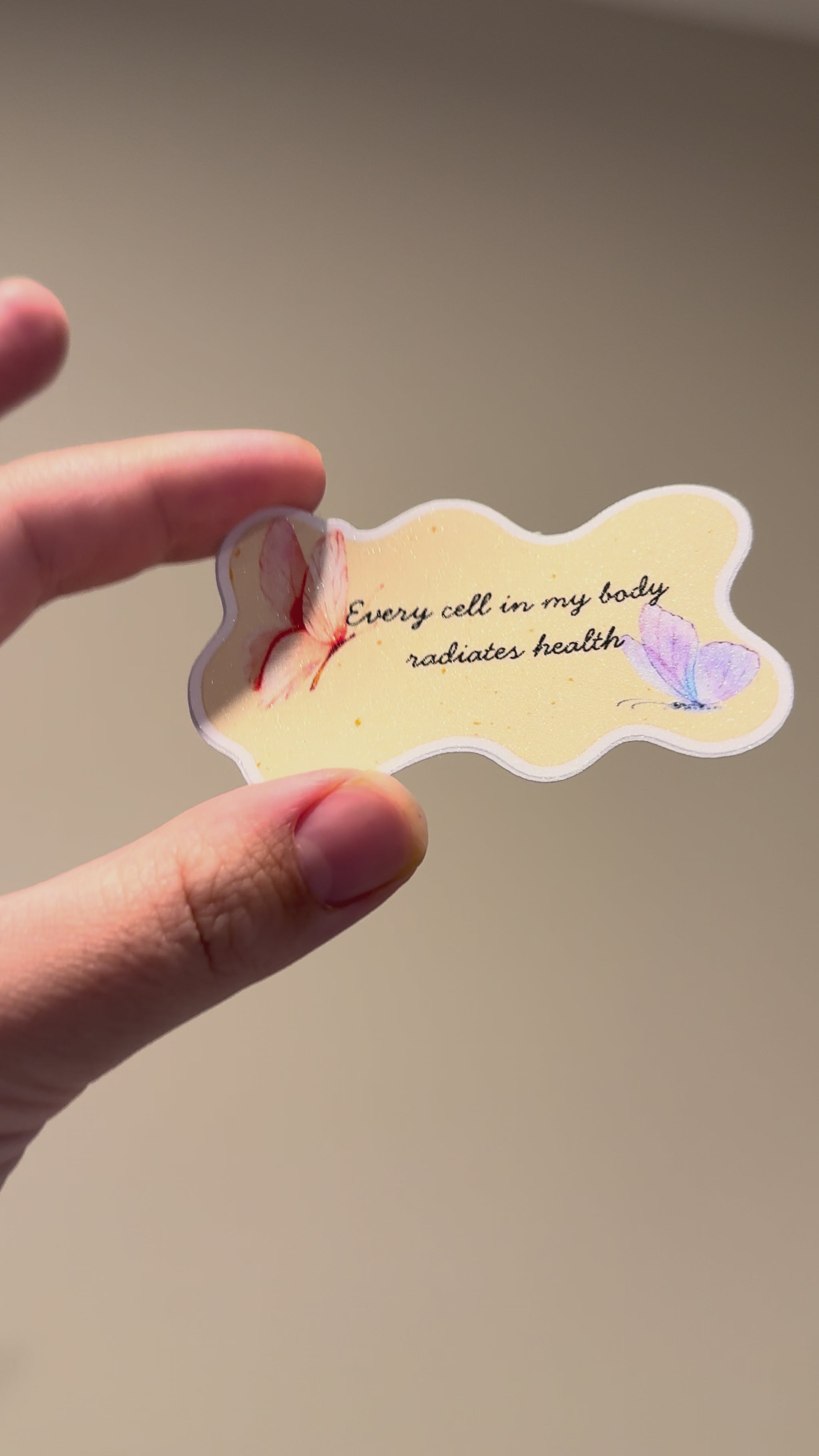 Close-up video of a watercolor butterfly affirmation sticker with glitter laminate, showcasing its shimmering finish, pastel butterfly artwork, and handmade details from multiple angles.