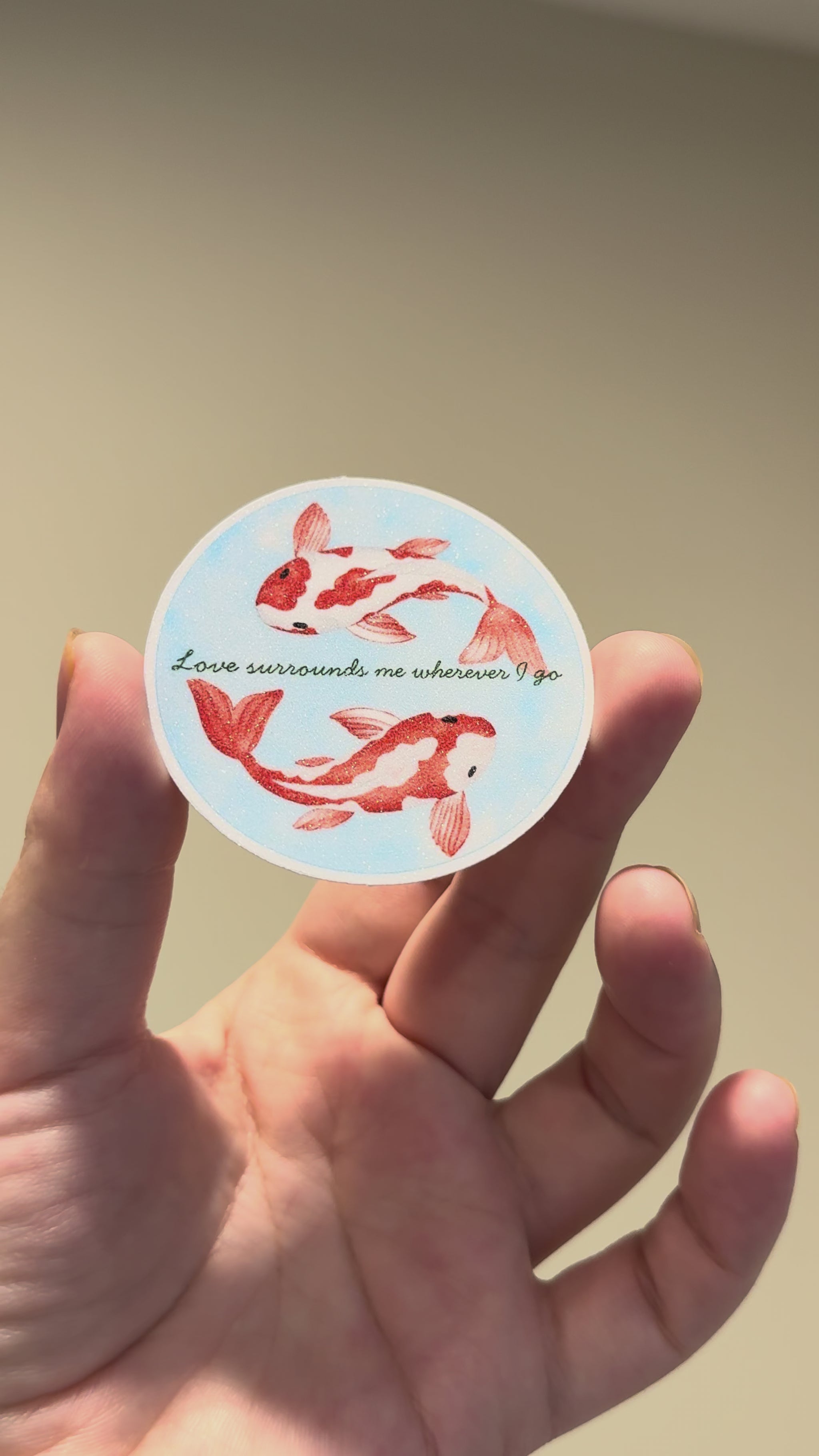 Close-up video of a watercolor koi fish affirmation sticker with glitter laminate, showcasing its sparkling finish, calming artwork, and handmade details from multiple angles.