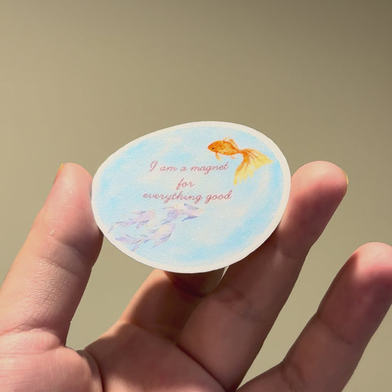 Close-up video of a blue watercolor fish affirmation sticker with glitter laminate, showing its sparkle and premium handmade finish from different angles.