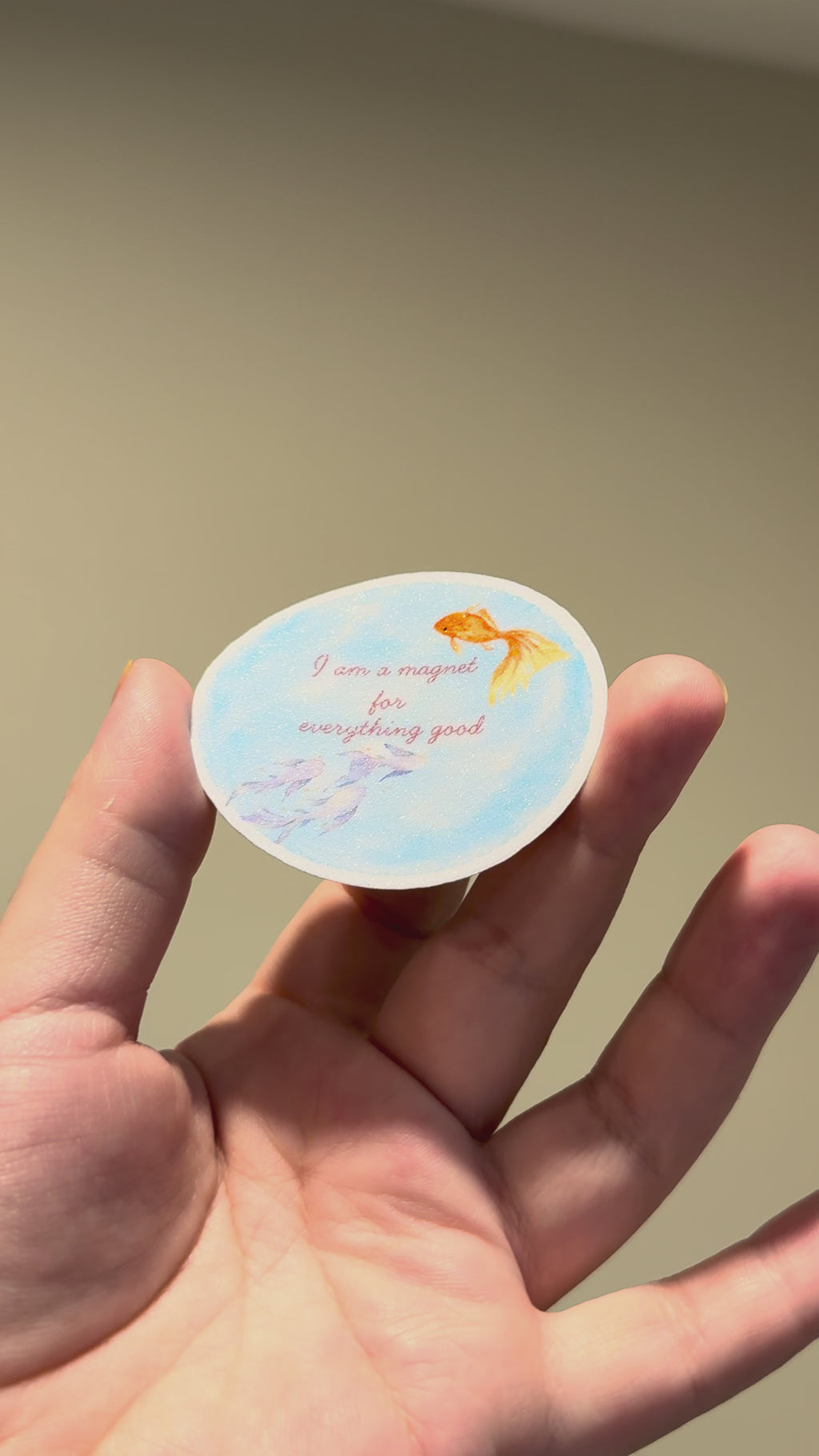 Close-up video of a blue watercolor fish affirmation sticker with glitter laminate, showing its sparkle and premium handmade finish from different angles.