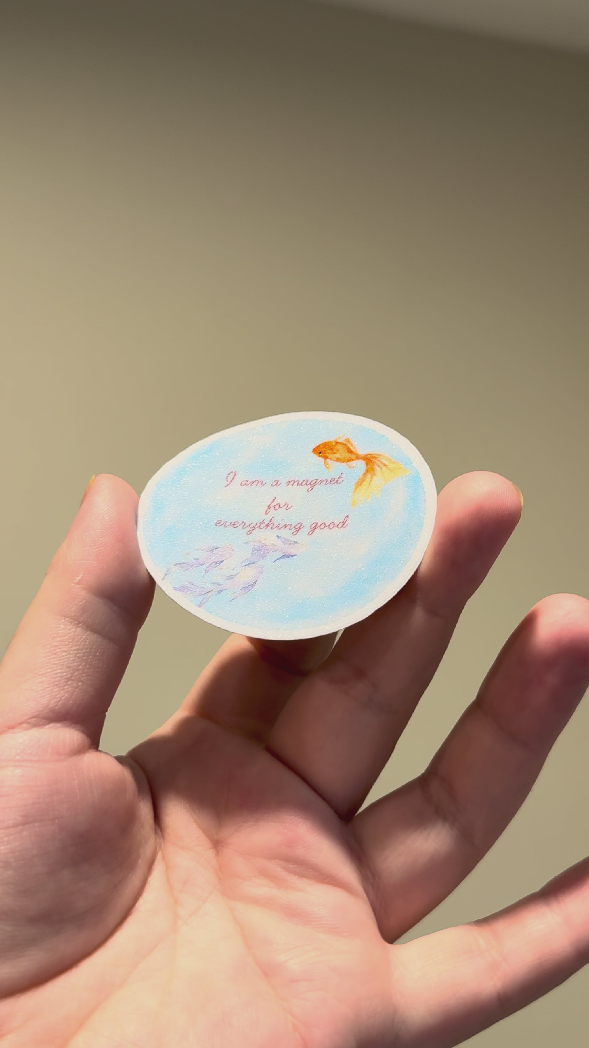 Close-up video of a blue watercolor fish affirmation sticker with glitter laminate, showing its sparkle and premium handmade finish from different angles.