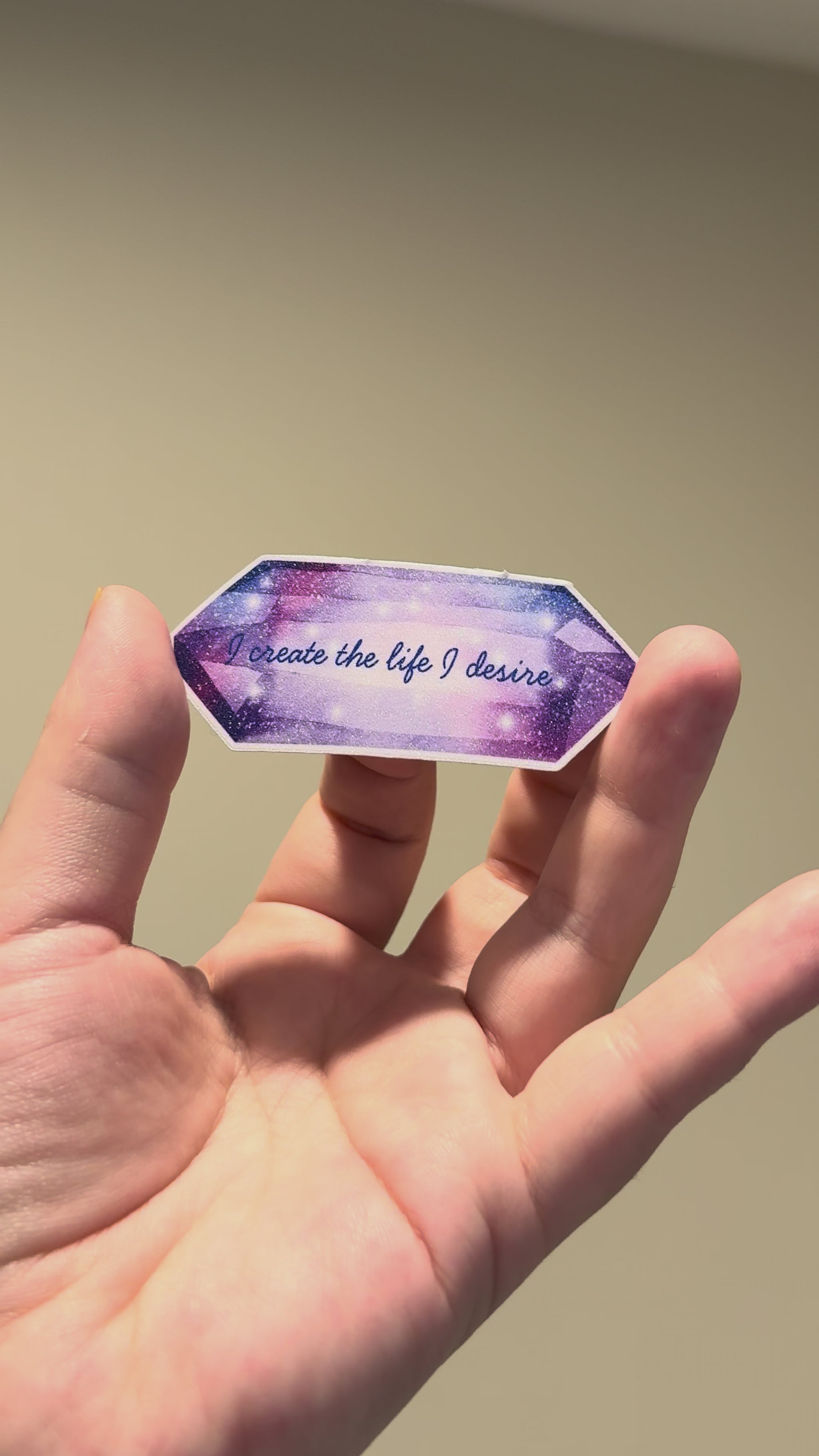 Close-up video of a purple crystal-inspired affirmation sticker with glitter laminate, highlighting its sparkling finish and premium handmade quality from different angles.
