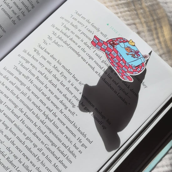 Book wrapped in scarf magnetic bookmark demo: cozy winter design clips onto book pages with strong magnet, shown on pink Keepsake House backing card
