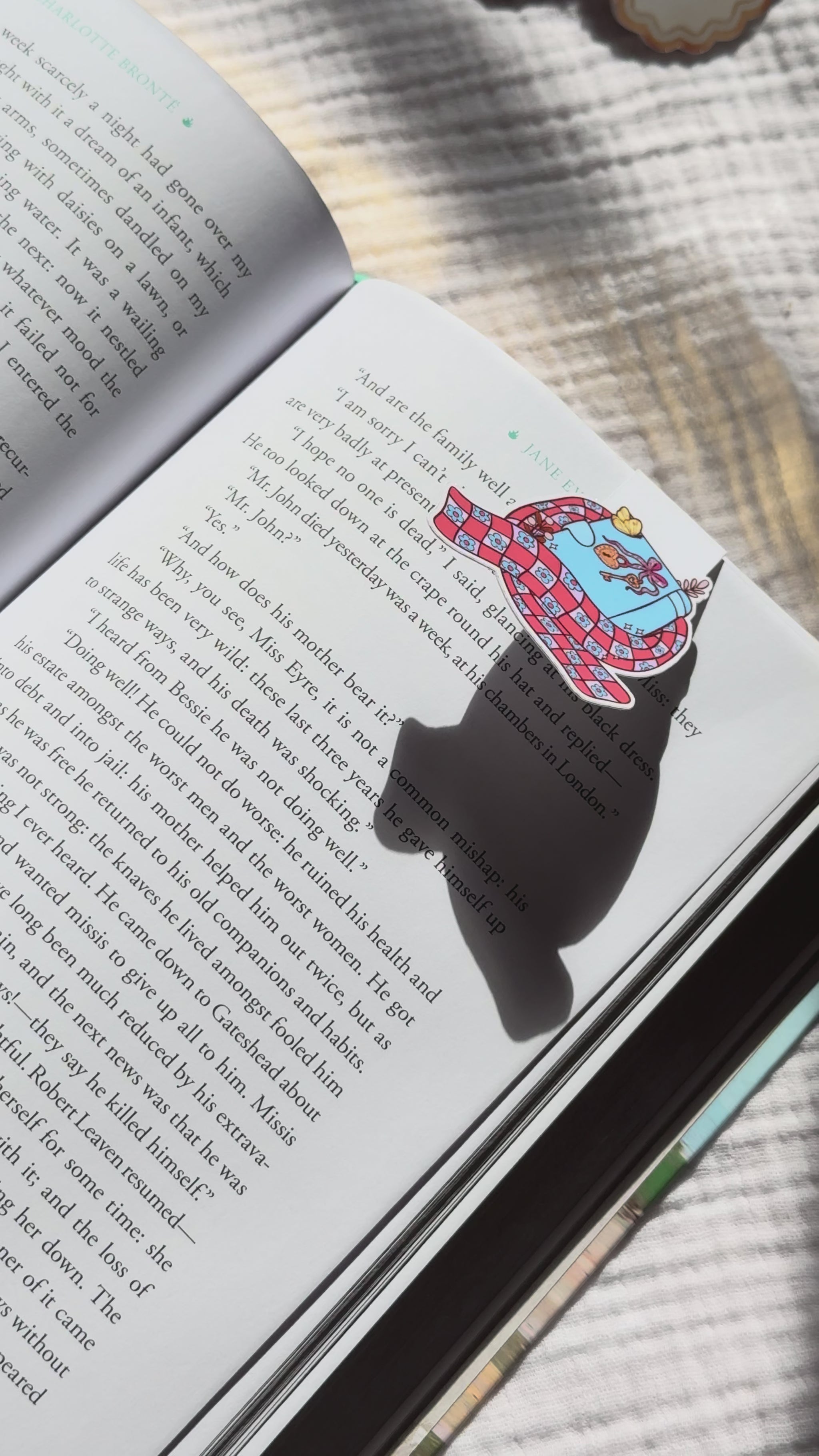Book wrapped in scarf magnetic bookmark demo: cozy winter design clips onto book pages with strong magnet, shown on pink Keepsake House backing card
